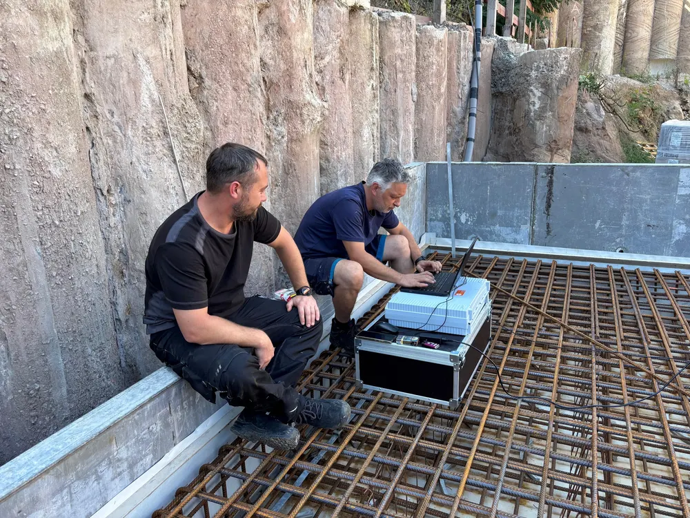 Zwei Monteure von E.N. mit Prüfkoffer und Laptop bei der Dichtheitsprüfung auf einer Baustelle